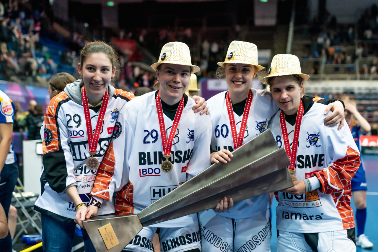 SWISS Arena (Kloten), 27.04.2019, Unihockey Damen NLA Superfinal, piranha chur - Kloten-Dietlikon Jets, Alina Räuftlin (Nr. 77, Kloten-Dietlikon Jets), Monika Schmid (Nr. 29, Kloten-Dietlikon Jets), Sara Tschudin (Nr. 60, Kloten-Dietlikon Jets) und Kim Buchs (Nr. 38, Kloten-Dietlikon Jets) mit dem Pokal
(Claudio Schwarz, unihockey-fotos.ch)
Copyright: Claudio Schwarz, unihockey-fotos.ch – Dieses Bild wurde durch swiss unihockey lizenziert und darf ausschliesslich auf den Online-Kanälen von swiss unihockey verwendet werden. Die redaktionelle oder kommerzielle Nutzung durch Dritte (Medien, Vereine, Unternehmen oder Privatpersonen) per Download von diesem flickr-Account ist ausgeschlossen. Das Bild kann bei Interesse via unihockey-fotos.ch kostenpflichtig lizenziert werden. unihockey-fotos.ch behält sich vor, fehlbaren Medien, Vereinen, Unternehmen oder Privatpersonen Bilder mit einem Zuschlag in Rechnung zu stellen.