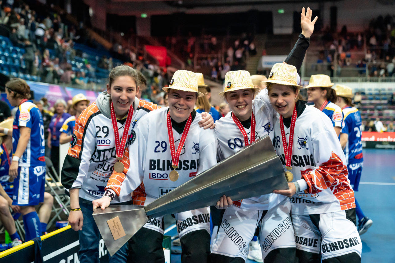 SWISS Arena (Kloten), 27.04.2019, Unihockey Damen NLA Superfinal, piranha chur - Kloten-Dietlikon Jets, Alina Räuftlin (Nr. 77, Kloten-Dietlikon Jets), Monika Schmid (Nr. 29, Kloten-Dietlikon Jets), Sara Tschudin (Nr. 60, Kloten-Dietlikon Jets) und Kim Buchs (Nr. 38, Kloten-Dietlikon Jets) mit dem Pokal
(Claudio Schwarz, unihockey-fotos.ch)
Copyright: Claudio Schwarz, unihockey-fotos.ch – Dieses Bild wurde durch swiss unihockey lizenziert und darf ausschliesslich auf den Online-Kanälen von swiss unihockey verwendet werden. Die redaktionelle oder kommerzielle Nutzung durch Dritte (Medien, Vereine, Unternehmen oder Privatpersonen) per Download von diesem flickr-Account ist ausgeschlossen. Das Bild kann bei Interesse via unihockey-fotos.ch kostenpflichtig lizenziert werden. unihockey-fotos.ch behält sich vor, fehlbaren Medien, Vereinen, Unternehmen oder Privatpersonen Bilder mit einem Zuschlag in Rechnung zu stellen.